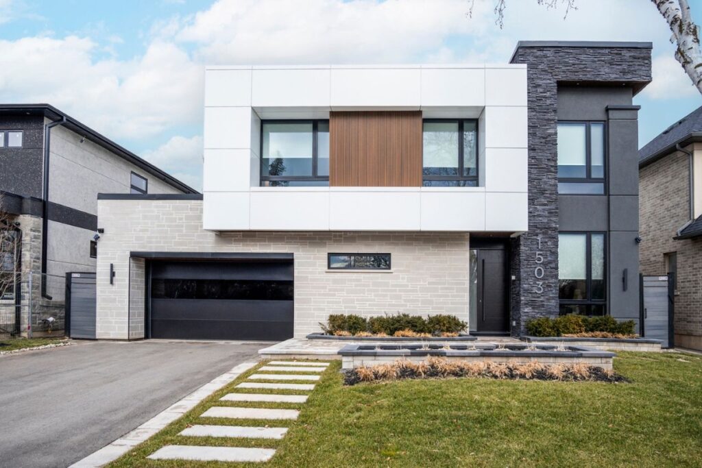 Modern two-story house with a flat roof, white and gray exterior, large windows, double garage, and a landscaped front yard with stone pavers and minimal shrubs.