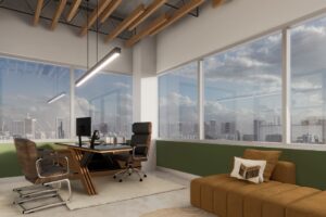 Modern office with large windows, city skyline view, wooden desk with computer, two office chairs, brown sofa, and exposed ceiling beams.