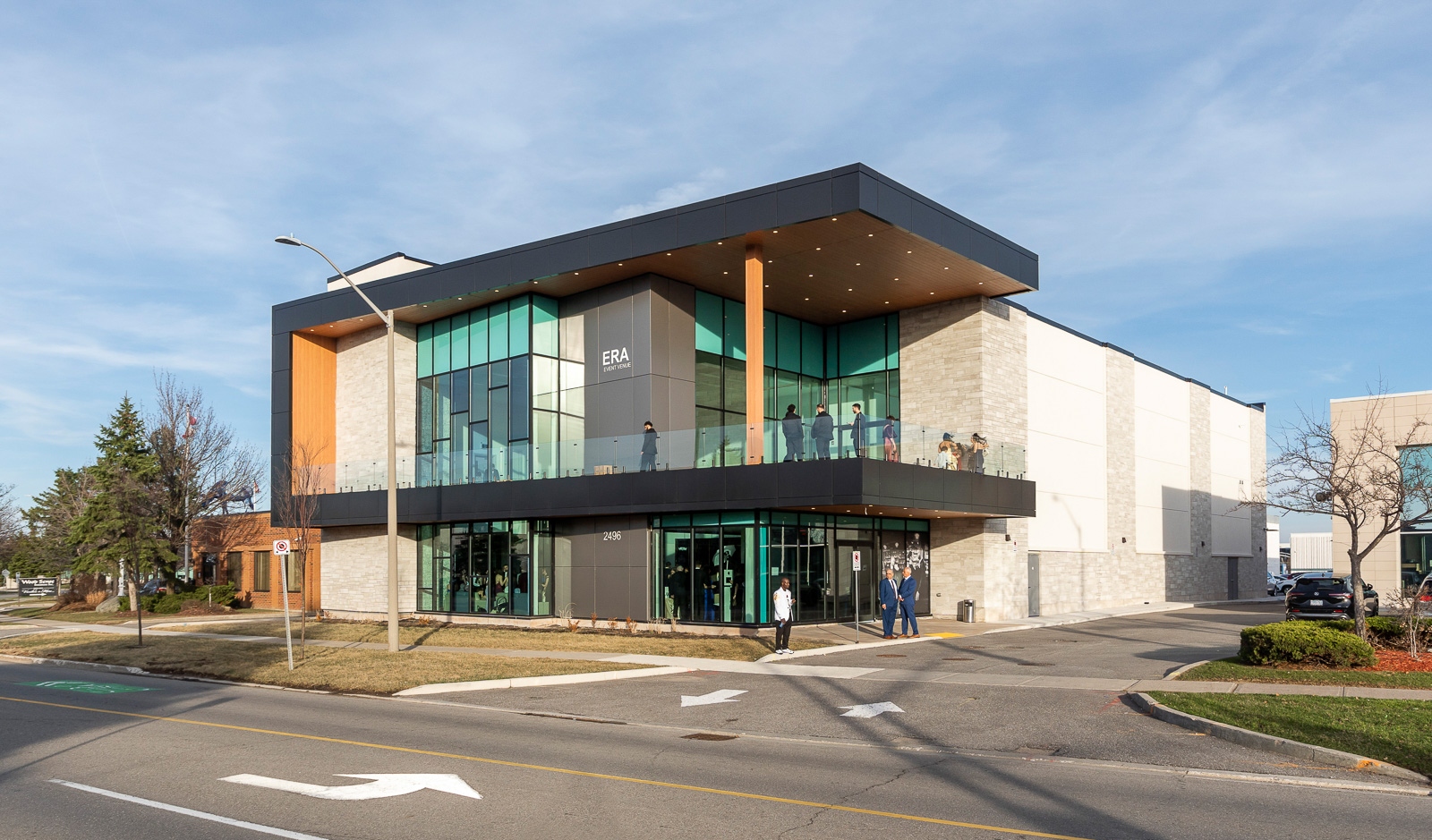 Modern two-story commercial building with large glass windows and a covered balcony on a street corner, with people walking near the entrance.