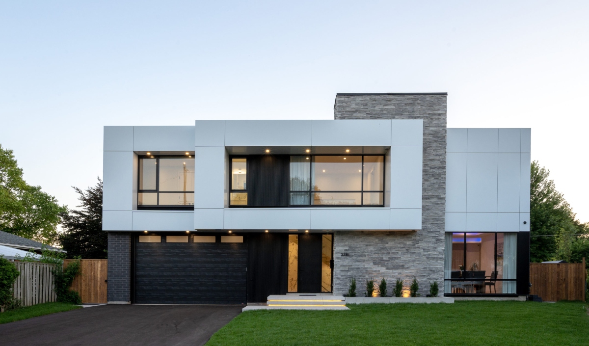 Modern custom home featuring two stories, large windows, a mix of stone and white panel exterior, dark garage door, and a neat green lawn in front.