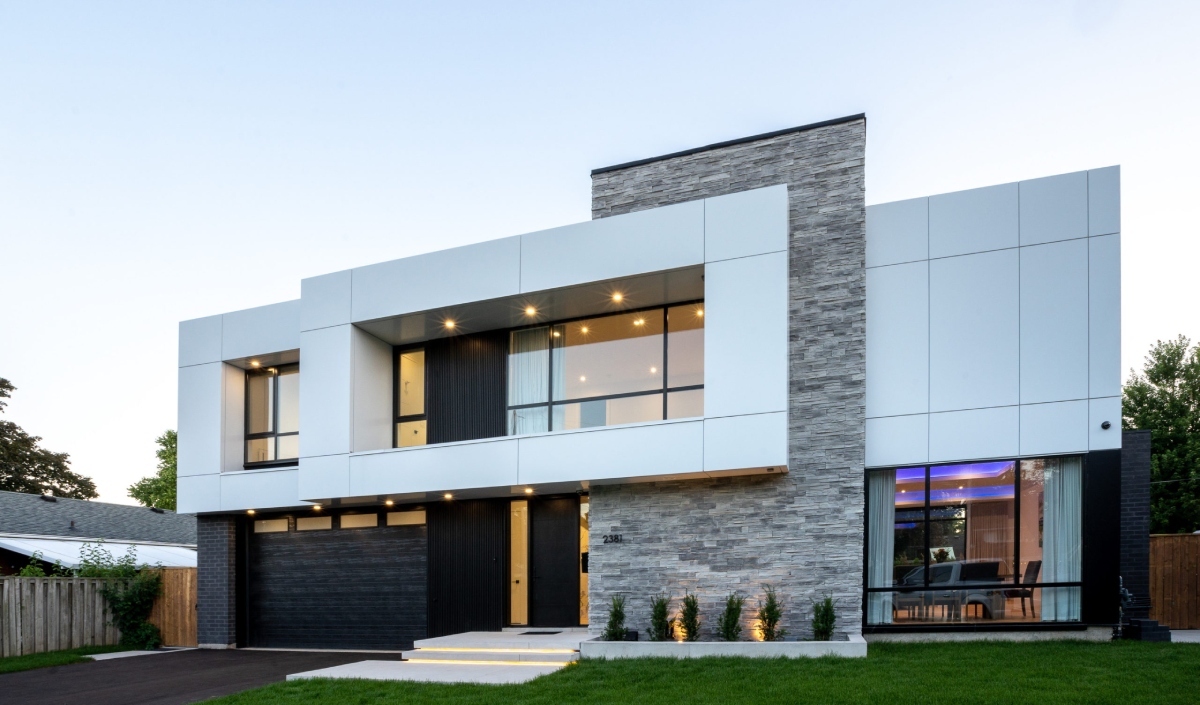 Modern Custom Home featuring a flat roof, large windows, white and gray exterior panels, stone accents, and a well-kept front lawn.