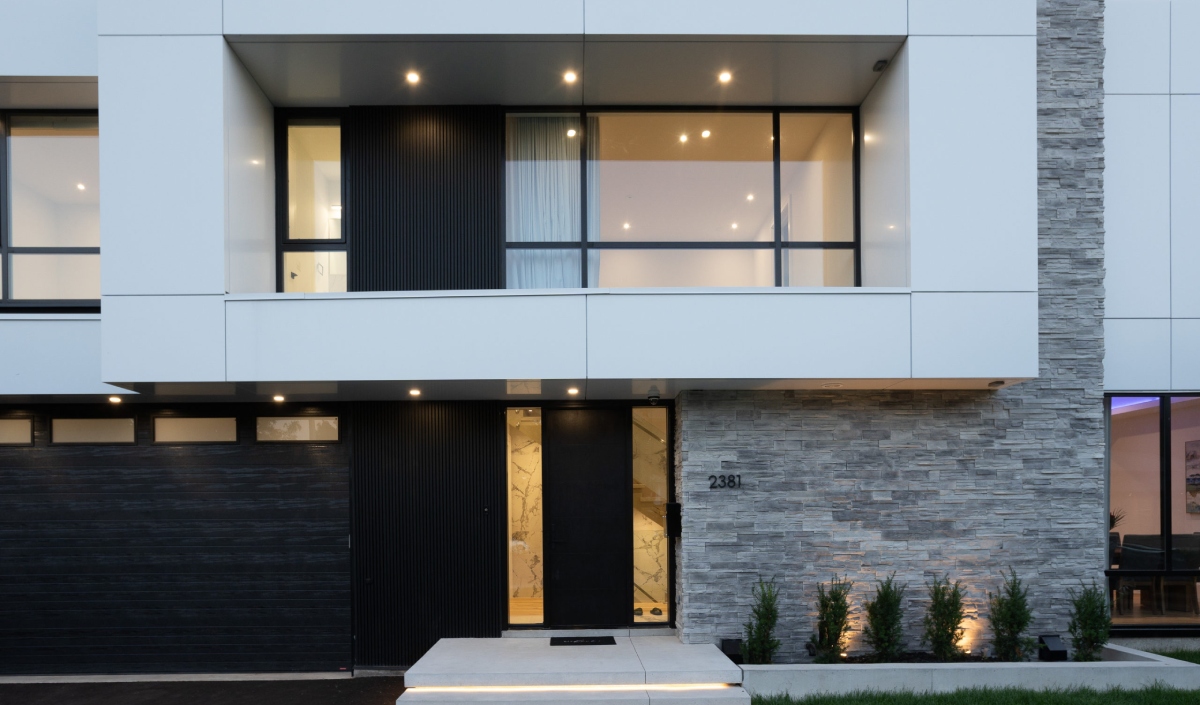 Modern Custom Home with a sleek two-story facade features large windows, white panels, stone accents, and a black front door next to the garage; small shrubs line the entrance walkway.