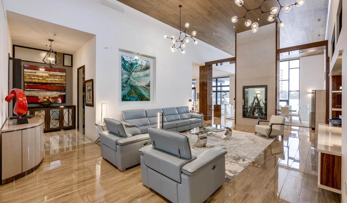 Modern living room with gray leather sofas, abstract artwork, marble floor, large windows, and contemporary light fixtures.