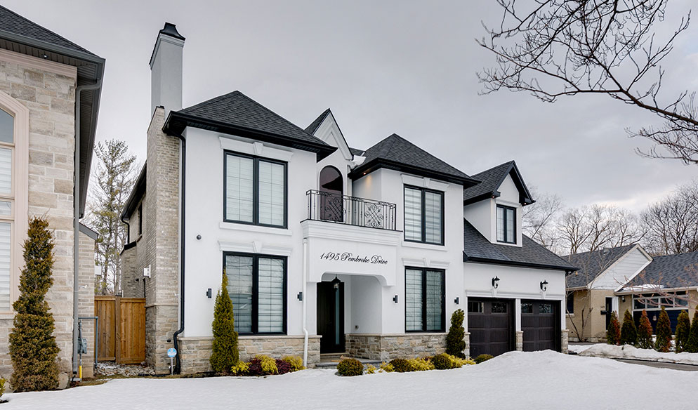 Two-story modern house with white exterior, black trim, and double garage; driveway and yard are covered in patches of snow.