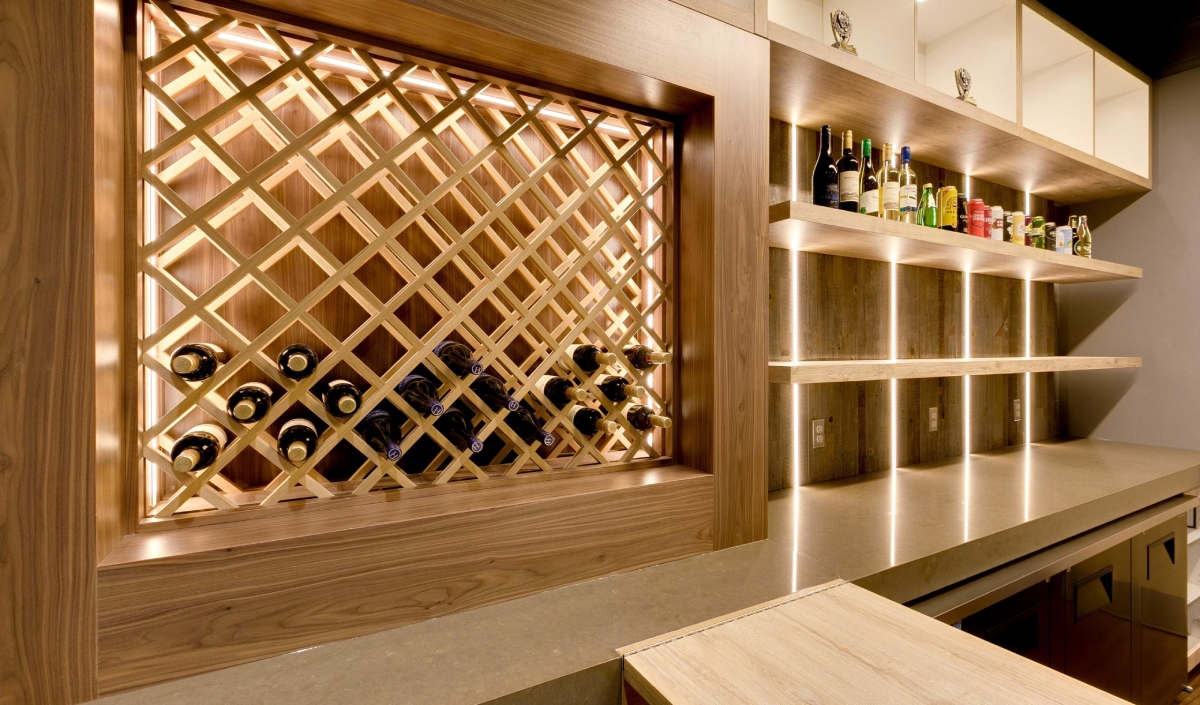 Modern wine cellar with wooden racks holding wine bottles, backlit shelves displaying various bottles, and a countertop beneath.
