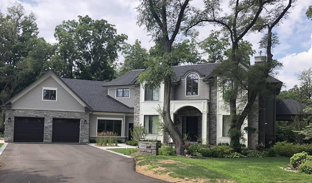 Two-story house with attached garage, stone and siding exterior, arched entryway, large windows, and trees in the front yard.