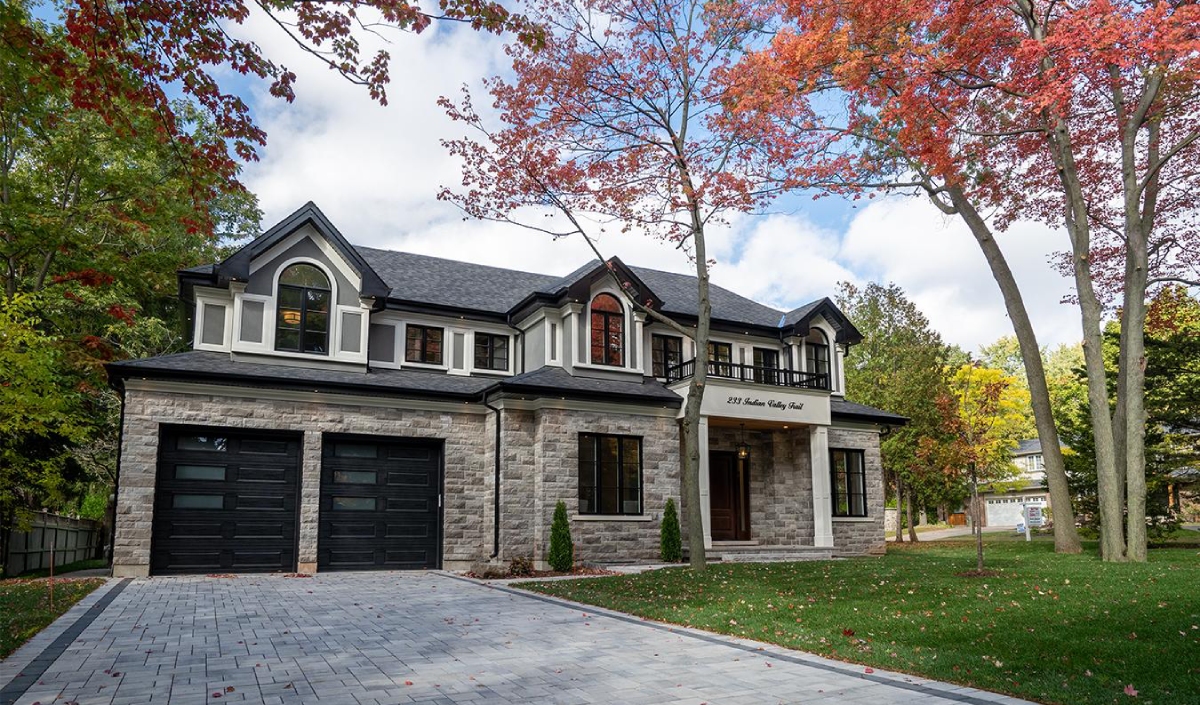 Two-story stone house with black double garage doors, arched windows, a paved driveway, and autumn trees in the front yard.