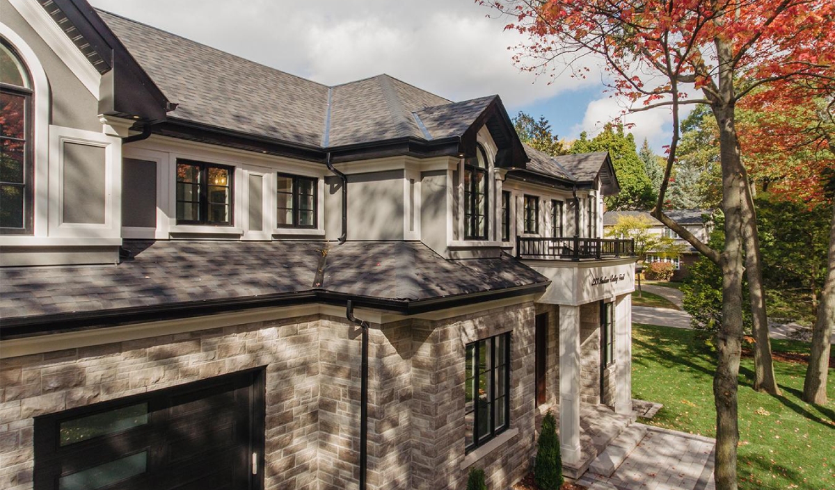 Two-story house with stone and stucco exterior, black-trimmed windows, and a balcony, surrounded by trees with autumn foliage.