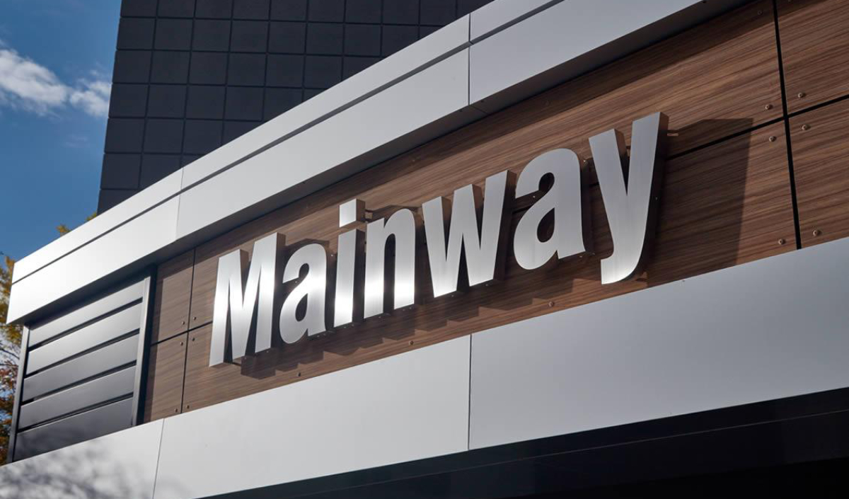 A building facade with a large, metallic sign reading "Mainway" mounted on a wood-paneled section.