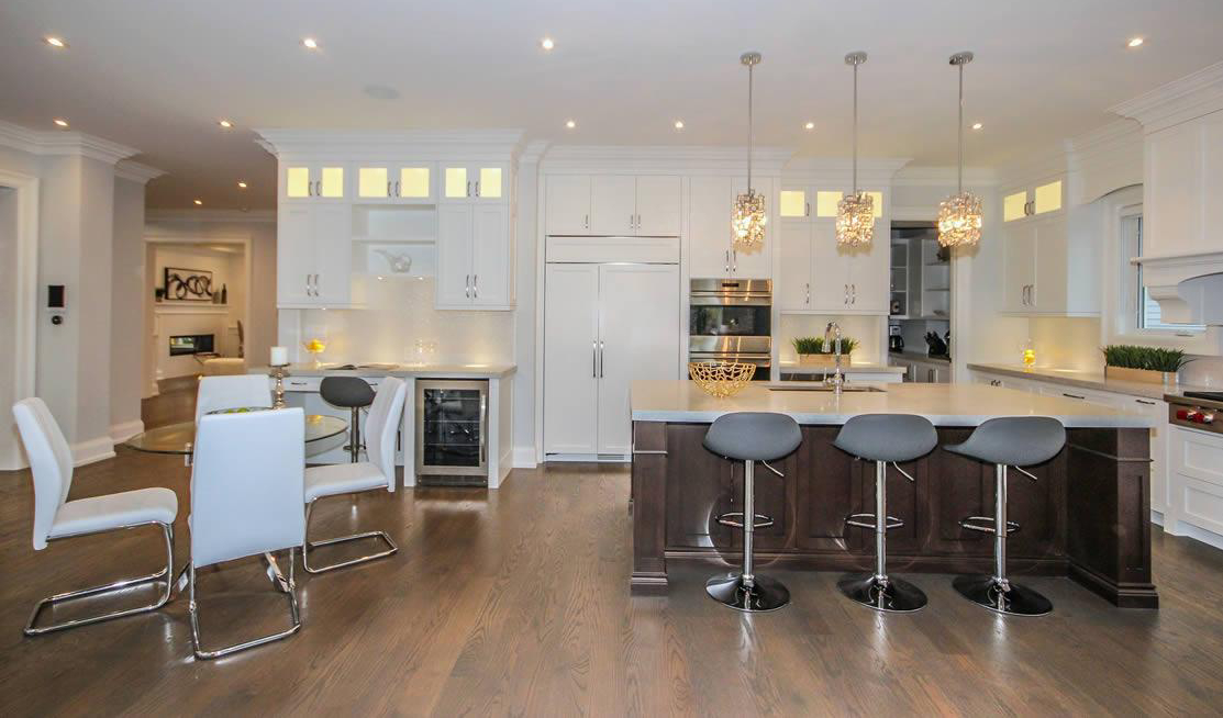 Modern kitchen with white cabinets, stainless steel appliances, a dark island with barstools, dining area with white chairs, and pendant lights over the island.
