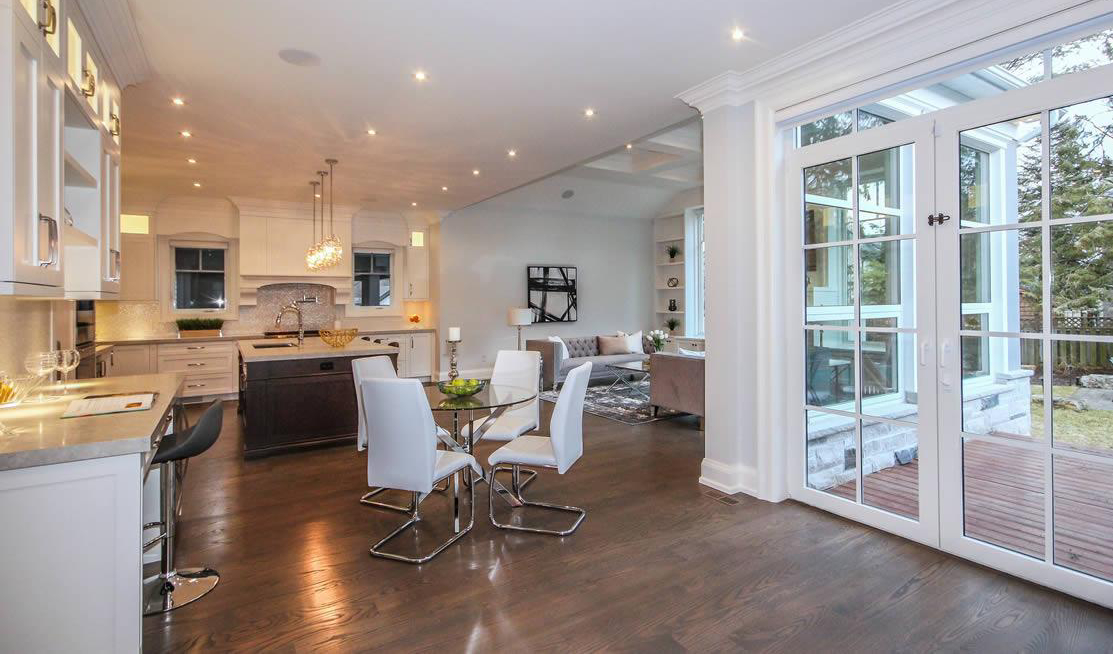 Modern open-concept kitchen and dining area with white cabinets, glass table, and sliding doors leading to a patio; adjacent living room visible in background.
