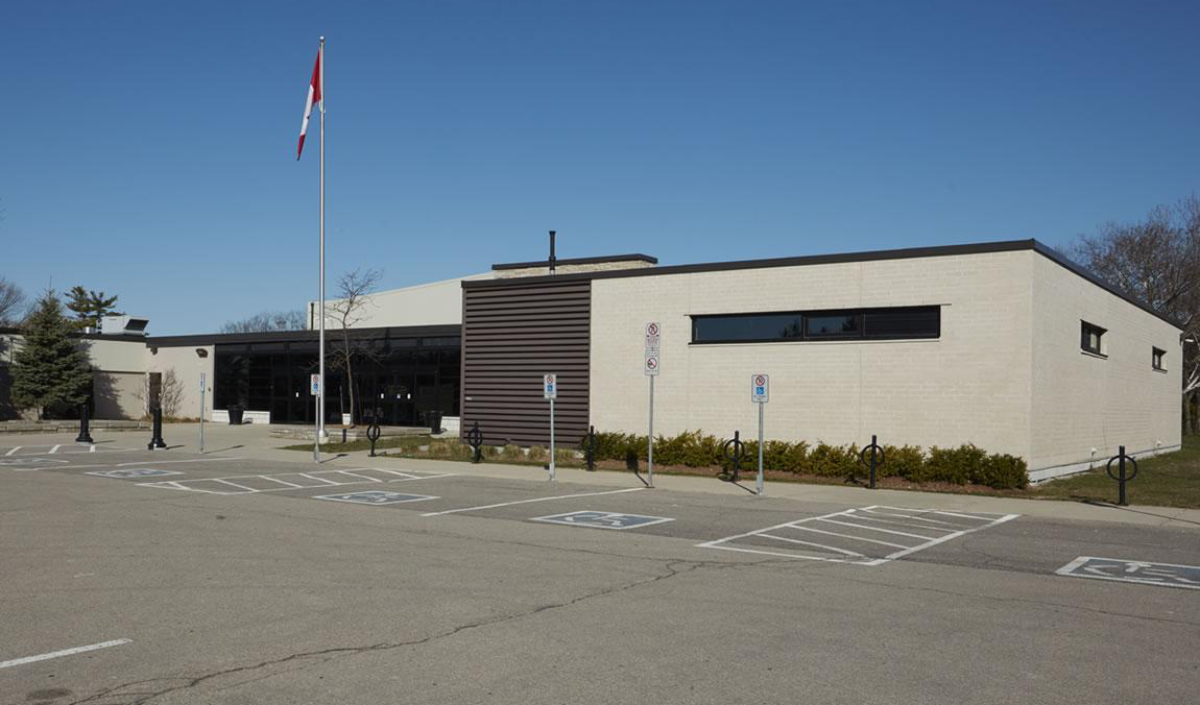 Single-story, modern public building with large windows, flagpole, and accessible parking spaces in front; clear sky and empty parking lot.
