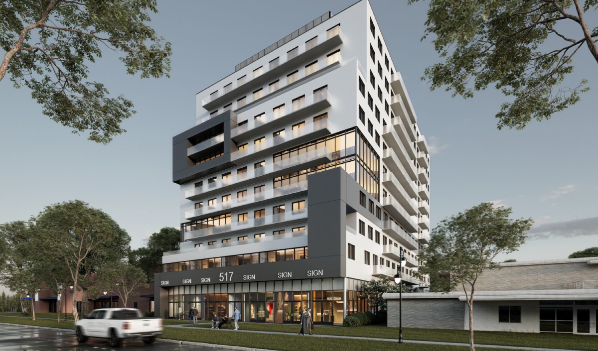 A modern multi-story apartment building with large windows and ground floor retail spaces, situated next to a street with trees and a parked white truck.