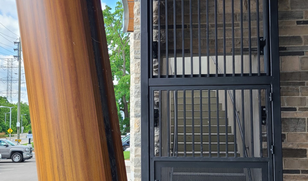 A black metal gate with vertical and horizontal bars blocks access to a stairwell beside a wooden pillar and a brick wall.