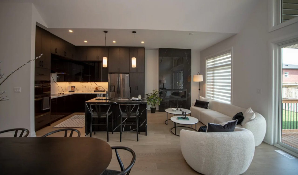 Modern open-concept kitchen and living area with dark cabinetry, marble island, white curved sofa, round coffee tables, and large windows providing natural light.