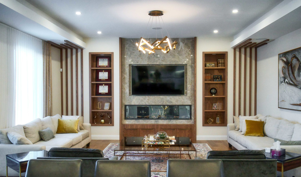 Modern living room with a large wall-mounted TV, built-in shelves, contemporary chandelier, sofas, glass coffee table, and decorative items.