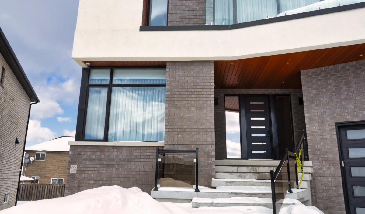 Modern two-story house with large windows, brick exterior, and snow-covered steps leading to a contemporary front door.