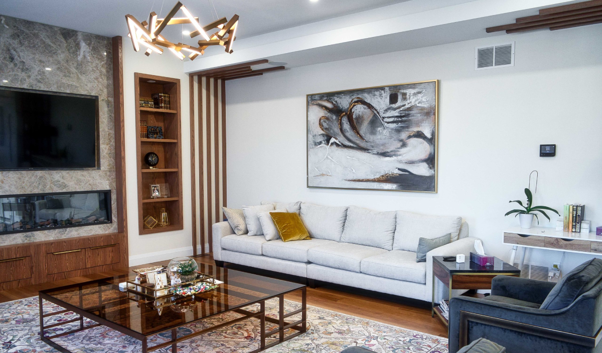 Modern living room with a gray sofa, abstract wall art, glass coffee table, built-in shelves, TV, and fireplace, featuring wooden and marble accents.