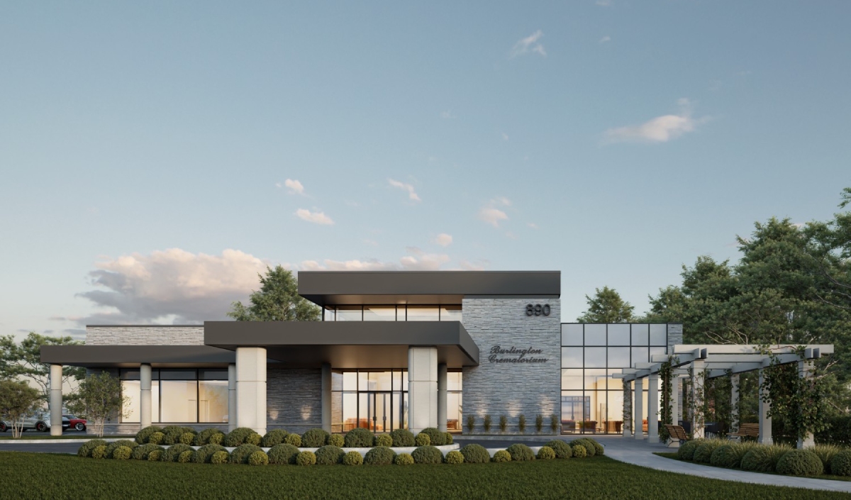 Modern building with large glass windows and a flat roof, surrounded by landscaped greenery and trees under a clear sky.