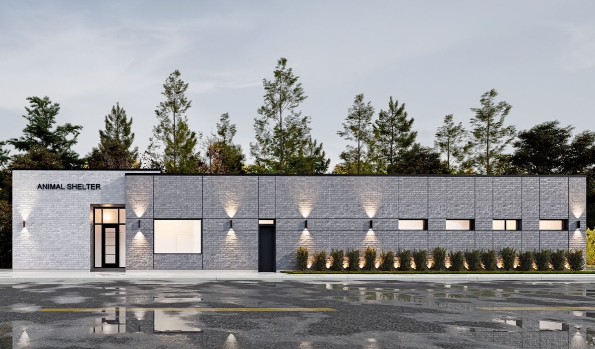 A modern, single-story animal shelter building with gray brick walls, exterior lighting, and trees in the background on a wet pavement.