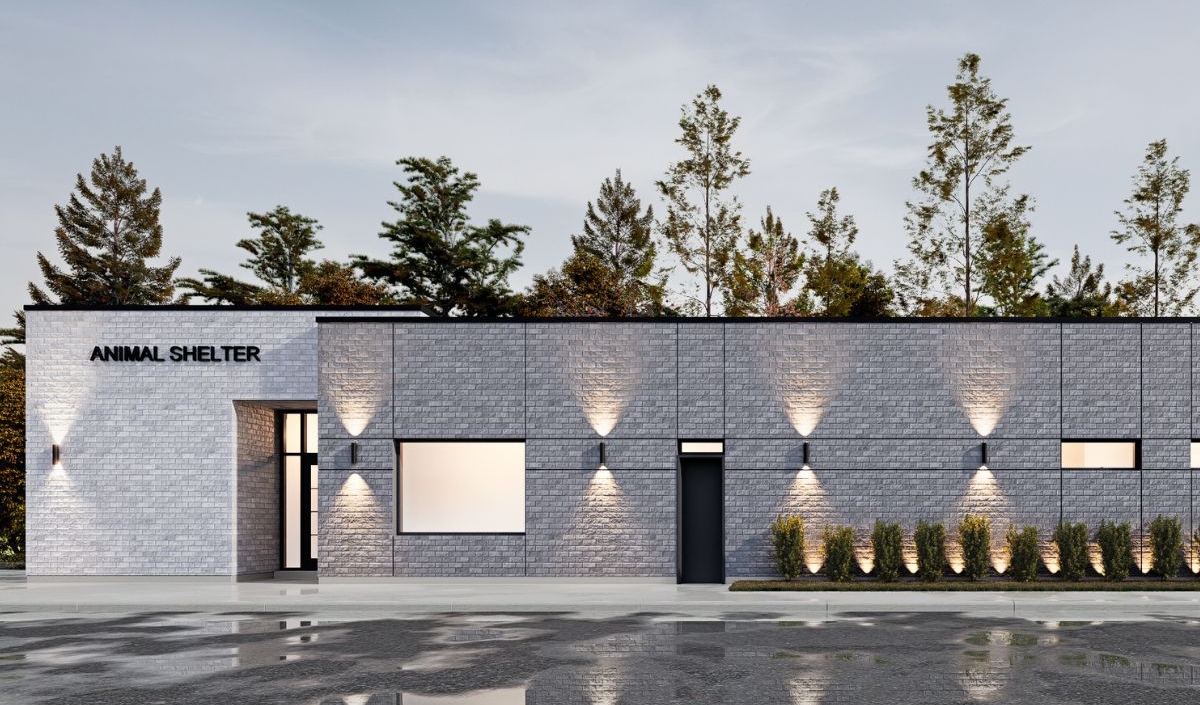 A modern, single-story animal shelter building with gray brick walls, large windows, and exterior lighting, set against a backdrop of trees.