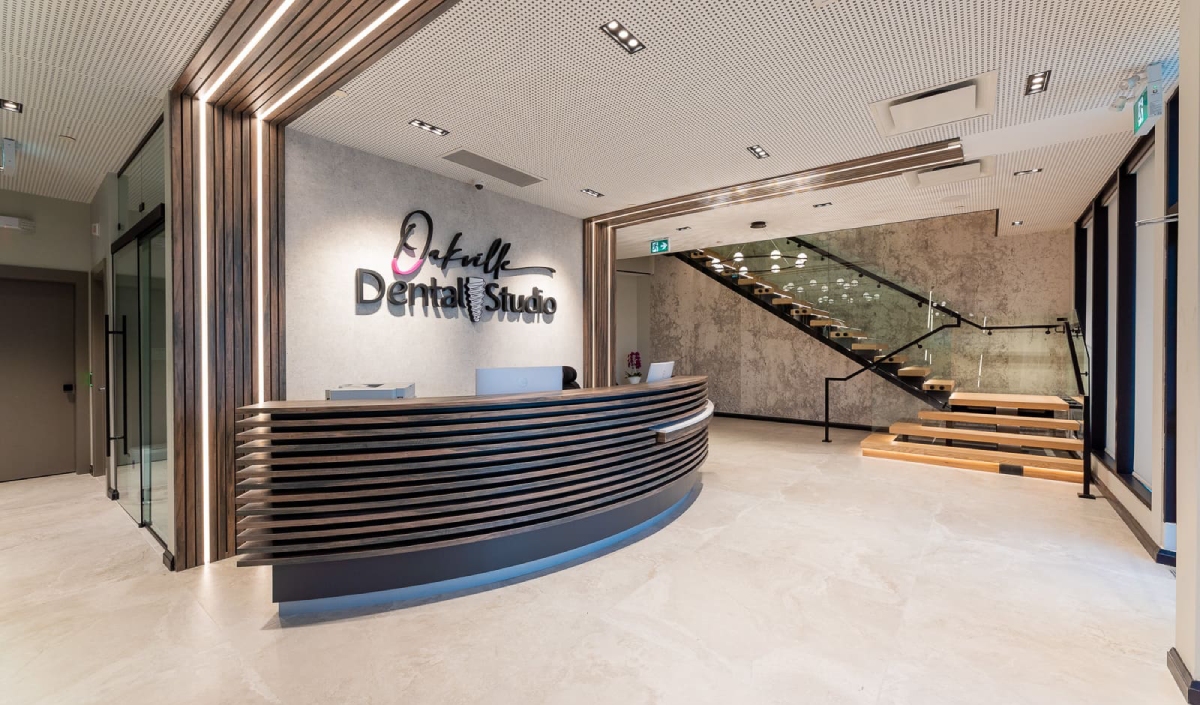 Reception area of a modern dental studio with a curved desk, logo on the wall, and a staircase with glass railing in the background.