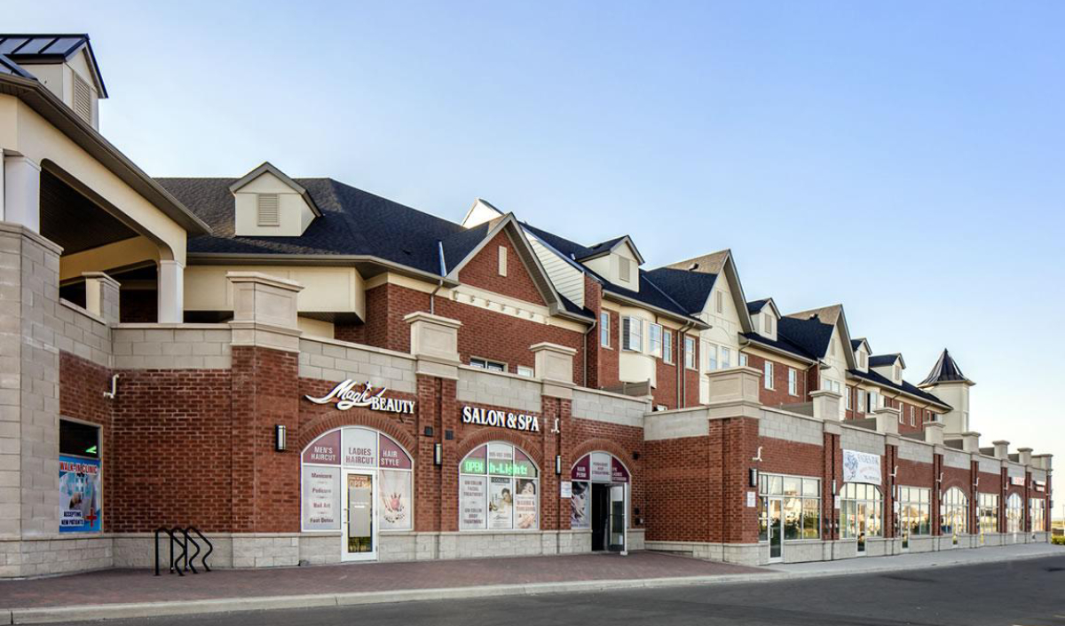 A modern brick commercial plaza with multiple storefronts, including a beauty salon and spa, under a clear sky.