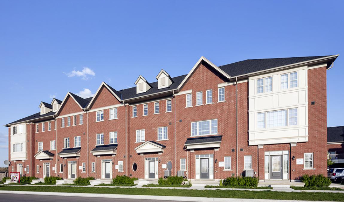A row of modern red brick townhouses with white trim, multiple stories, and gabled roofs under a clear blue sky.