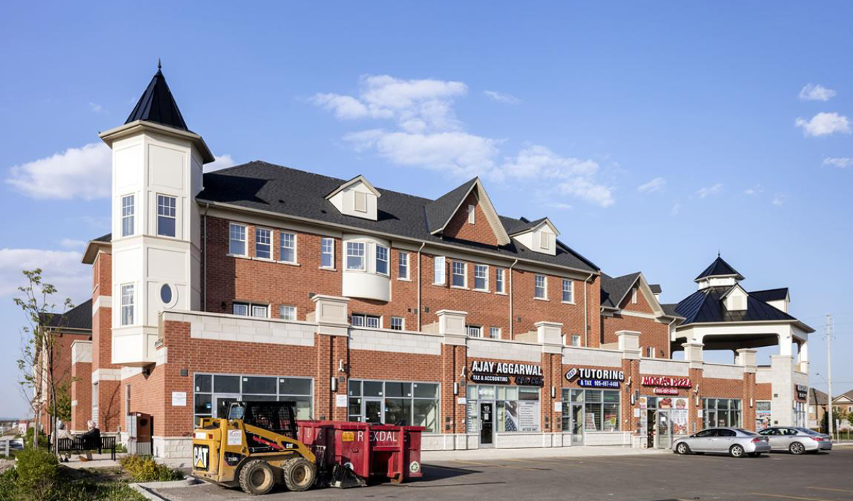 A modern red-brick commercial building with shops and tutoring services on the ground floor, parking area, and construction equipment in front.