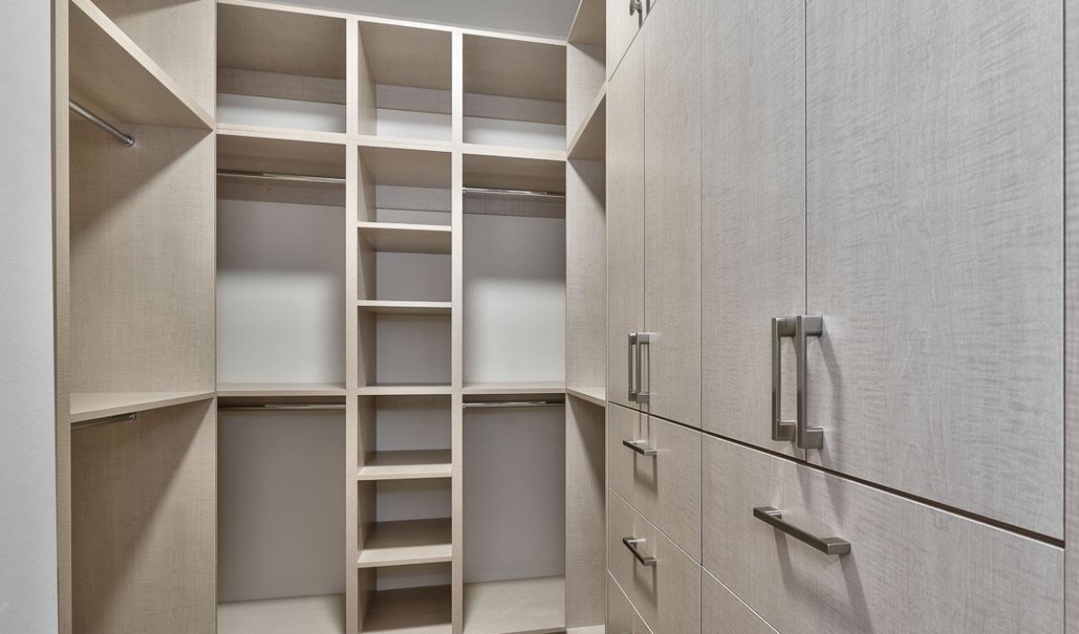 A modern walk-in closet with light wood cabinetry, multiple shelves, hanging rods, and drawers, all empty and neatly arranged.