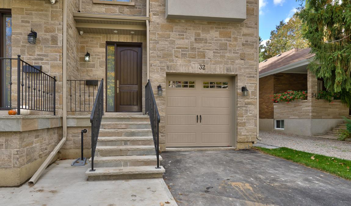 Front view of a house with a stone exterior, a dark brown door at the top of concrete steps, and a single-car garage with beige doors labeled with the number 32.